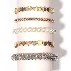 Set of 5 gold beaded bracelets with heart and star charms on a pink display stand