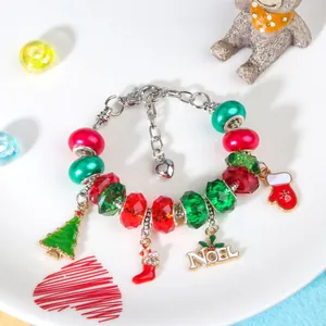 Kerst DIY bedelarmband met rode en groene kralen en zilveren hangers op een wit bord
