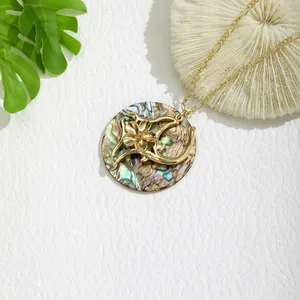 Macro detail of round gold pendant with natural shell inlay and floral cut-outs