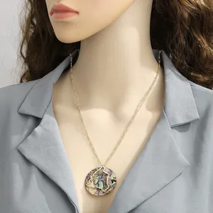 Detail of round gold pendant necklace with shell inlay worn over a grey blazer
