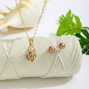 Detailliertes Perlen-Schmuckset mit Käfig-Anhänger und Ohrringen auf einem Seil vor Muschel