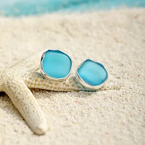 Minimalistische Meerglas-Ohrstecker mit Silberrand auf weißem Sand mit Seestern