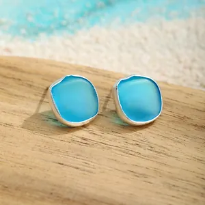 Makroaufnahme von blauen Meeresglas-Ohrringen mit Silberrand auf Holzoberfläche