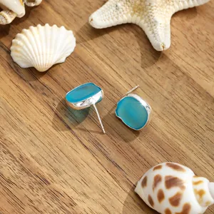 Nahaufnahme der blauen Meeresglas-Ohrringe auf Holz mit Seesternen und Muscheln