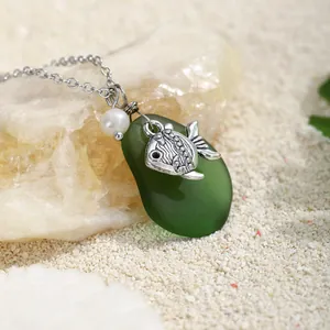 Dettaglio di una collana a tema marino con charm in vetro di mare verde e ciondolo a pesce