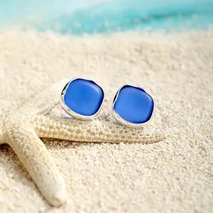 Nahaufnahme der blauen Meeresglas-Ohrringe auf weißem Sandstrand mit einem Seestern