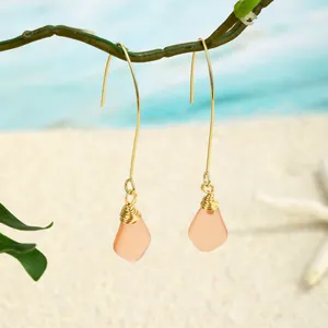 Details handgefertigter Ohrringe aus Golddraht und orangefarbenem Seeglas am Strand