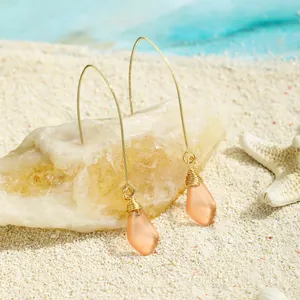 Handgefertigte Meerglas-Ohrhänger mit Golddrahtwickelung auf weißem Sandstrand-Hintergrund