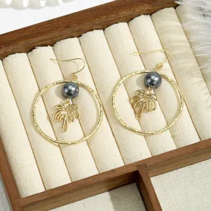 Détail de boucles d'oreilles créoles dorées avec pendentif palmier et perle grise