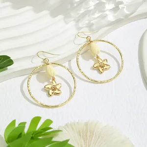 Détail de boucles d'oreilles créoles dorées avec pétales évidés et accents de perles