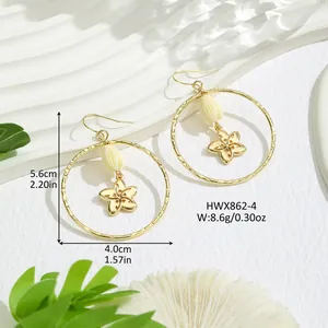 Détail de créoles géométriques dorées avec pendentifs de fleurs perlées sur fond coquillage