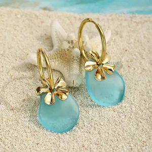 Detailansicht der Seeglas-Ohrringe mit Goldblumen auf weißem Sand und Seestern