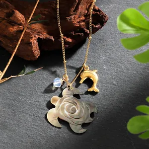 Hawaiian shell turtle necklace with golden dolphin pendant and blue bead on stone background