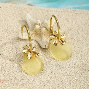 Gelbe Meeresglas-Ohrringe mit goldenem Blumenverschluss auf weißem Sand im Detail