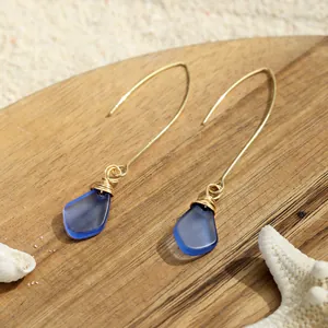 Detailansicht handgefertigter Seeglas-Ohrringe mit Golddrahtwicklung auf Sand und Muscheln