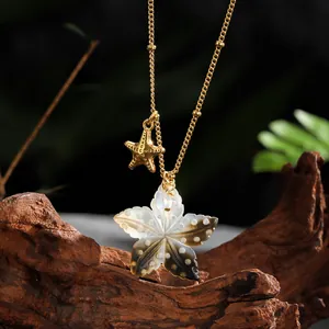 Close-up of a gold starfish and shell leaf pendant on dark wood, beach jewelry style