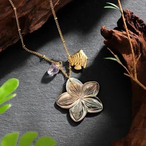 Detail of shell flower necklace with gold fish charm and purple gemstone on slate
