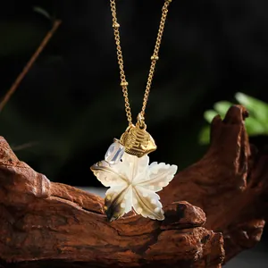 Macro view of a gold maple leaf shell pendant necklace with a blue bead on a wooden block