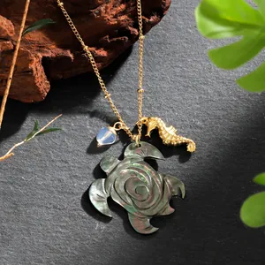 Detail of golden turtle necklace with iridescent mother of pearl shell and seahorse charm