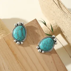 Détail de boucles d'oreilles turquoise en goutte avec perles argentées sur bois