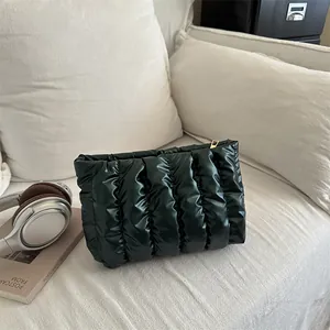 Borsa da trucco trapuntata verde scuro con cerniera dorata su sfondo in tessuto