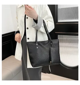 Detail van zwarte gevlochten shopper met bijpassende kleine tas op een witte jas