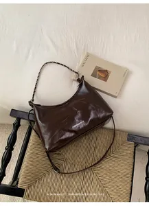 Detail of dark brown glossy leather hobo bag with chain strap on a vintage woven chair