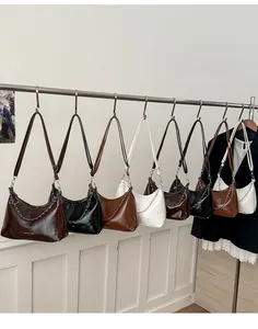 Crescent tote bags in various colors hanging with silver chain detail on a metal rod