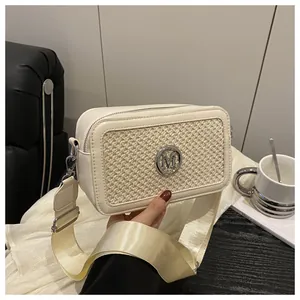 Detail of cream woven leather camera bag with silver M logo and wide strap on desk