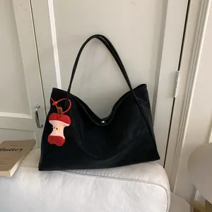 Minimalist black soft leather tote bag with apple plush pendant on a beige sofa