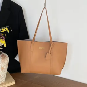 Brown leather large tote bag with shoulder straps and gold lettering on white wall