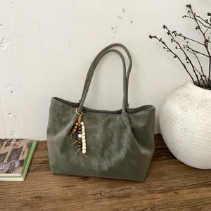 Grüne Wildleder-Tragetasche mit Retro-Perlen-Quaste auf einer Holzbank im minimalistischen Stil