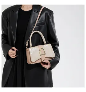 Détail du sac beige avec boucle en U dorée porté sur un blazer en cuir noir élégant