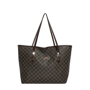 Large tote bag with M-pattern print and gold bow hardware on a white background