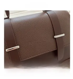 Détail du sac messager en cuir marron texturé avec des boucles métalliques argentées