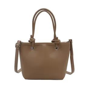 Brown minimalist PU leather tote bag with knot handle and adjustable strap in white background