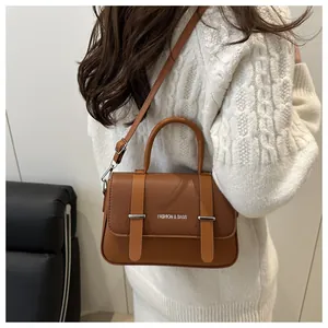 Petit sac boîte marron avec logo argenté porté sur un pull en maille torsadée crème