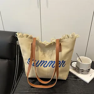 Beige canvas summer tote bag with blue embroidery and brown leather straps on a table