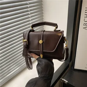 Vintage dark brown crossbody bag with gold hardware shown in a hand-held fashion pose