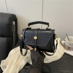 Retro black leather crossbody bag with gold buckle and handle shown in a modern setting