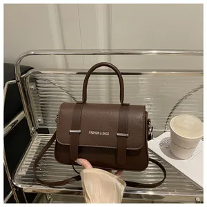 Detalle de bolso de cuero marrón oscuro con correas decorativas en soporte transparente