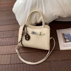 Beige handtas met leertextuur, crossbody riem en creatieve hanger in de vorm van een pretzel