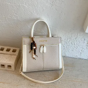 Bolso bandolera beige texturizado con ribete de cuero y colgante de cuentas de madera