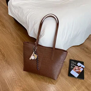 Large dark brown crocodile embossed tote bag with baseball charm on wooden floor