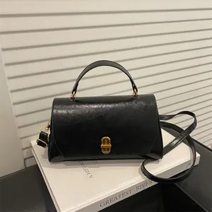 Retro black leather handbag with gold metal lock on white books, versatile crossbody bag