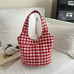 Red and white plaid canvas tote bag with front pockets on a white sofa setting