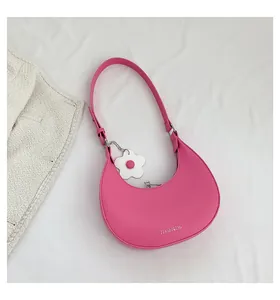 Detailed view of pink crescent bag with white floral charm and adjustable shoulder strap