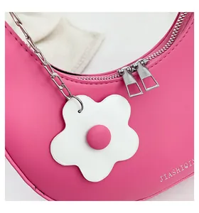 Detail of pink half-moon bag with silver zippers and a white flower charm accessory