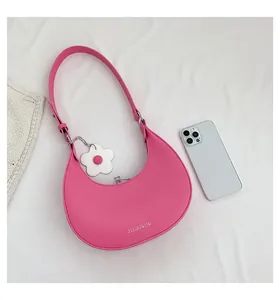 Pink crescent shoulder bag with white flower charm and zipper detail on fabric background