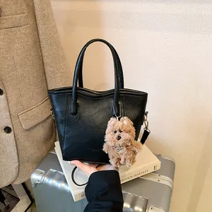 Minimalist black leather tote bag with plush puppy pendant and dual straps for daily commute